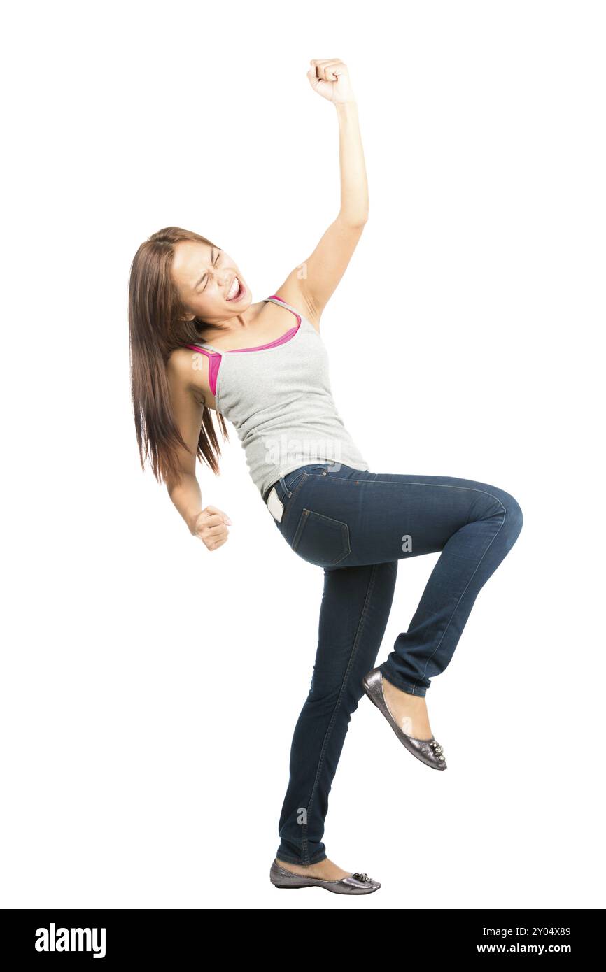 Donna asiatica dall'aspetto estatico, con jeans casual e canotta, occhi chiusi, urla, festeggia e vince alzando il pugno in t Foto Stock