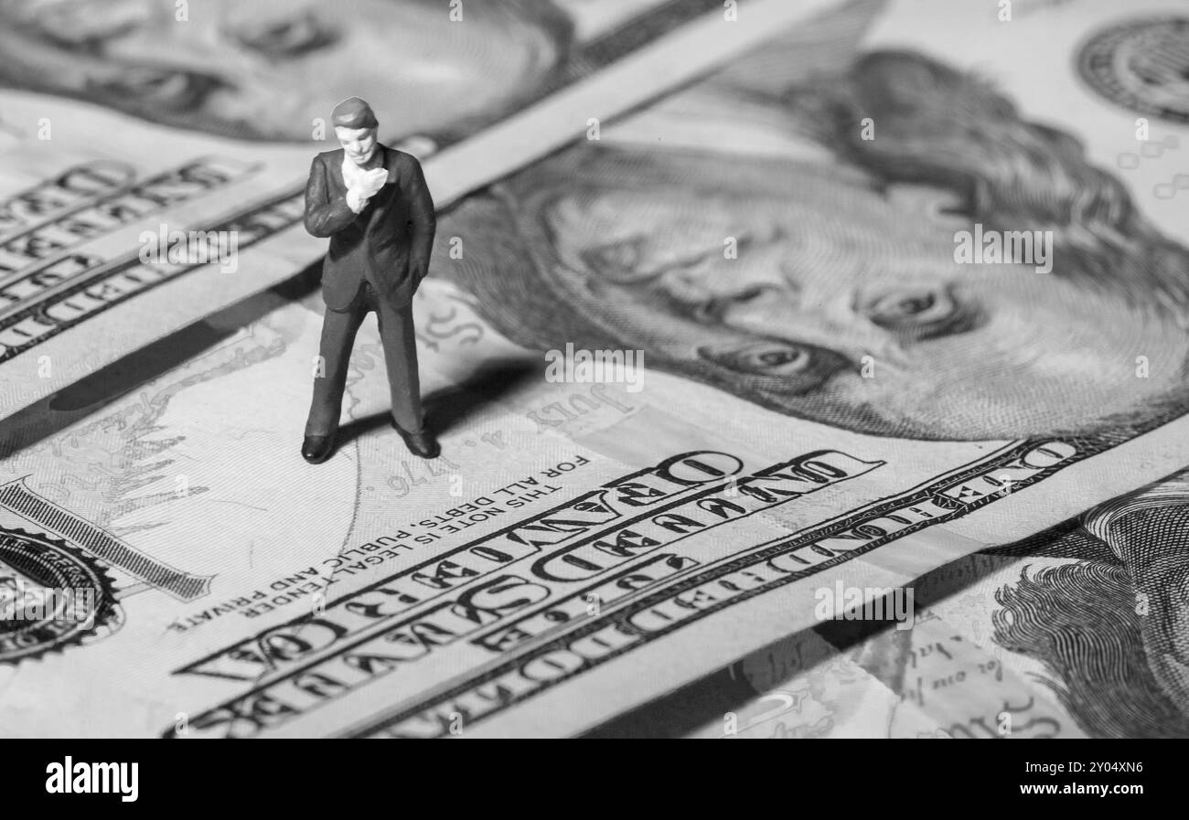 Uomo d'affari in miniatura con banconota da 100 dollari sullo sfondo. Concetto Foto Stock