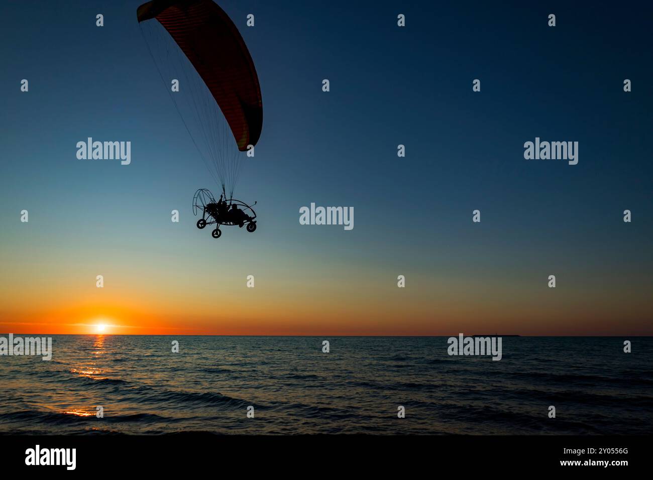 Una persona si sta godendo l'esperienza emozionante di paracadutismo ascensionale sopra lo scintillante oceano sotto i colori vibranti di un bellissimo tramonto Foto Stock