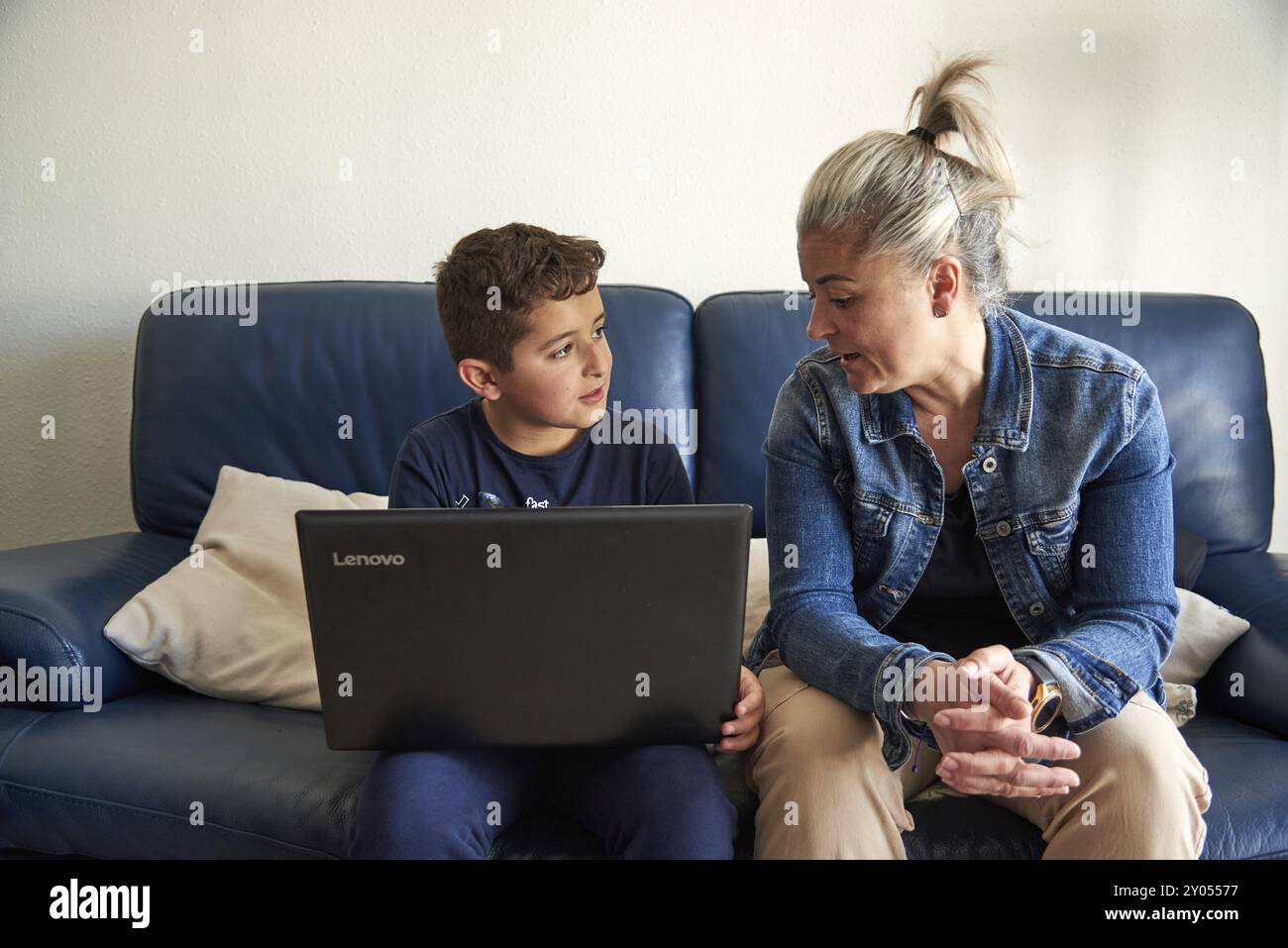 Madre e figlio sono seduti su un divano blu, impegnati in una conversazione mentre guardano un computer portatile, nel salotto di casa loro Foto Stock