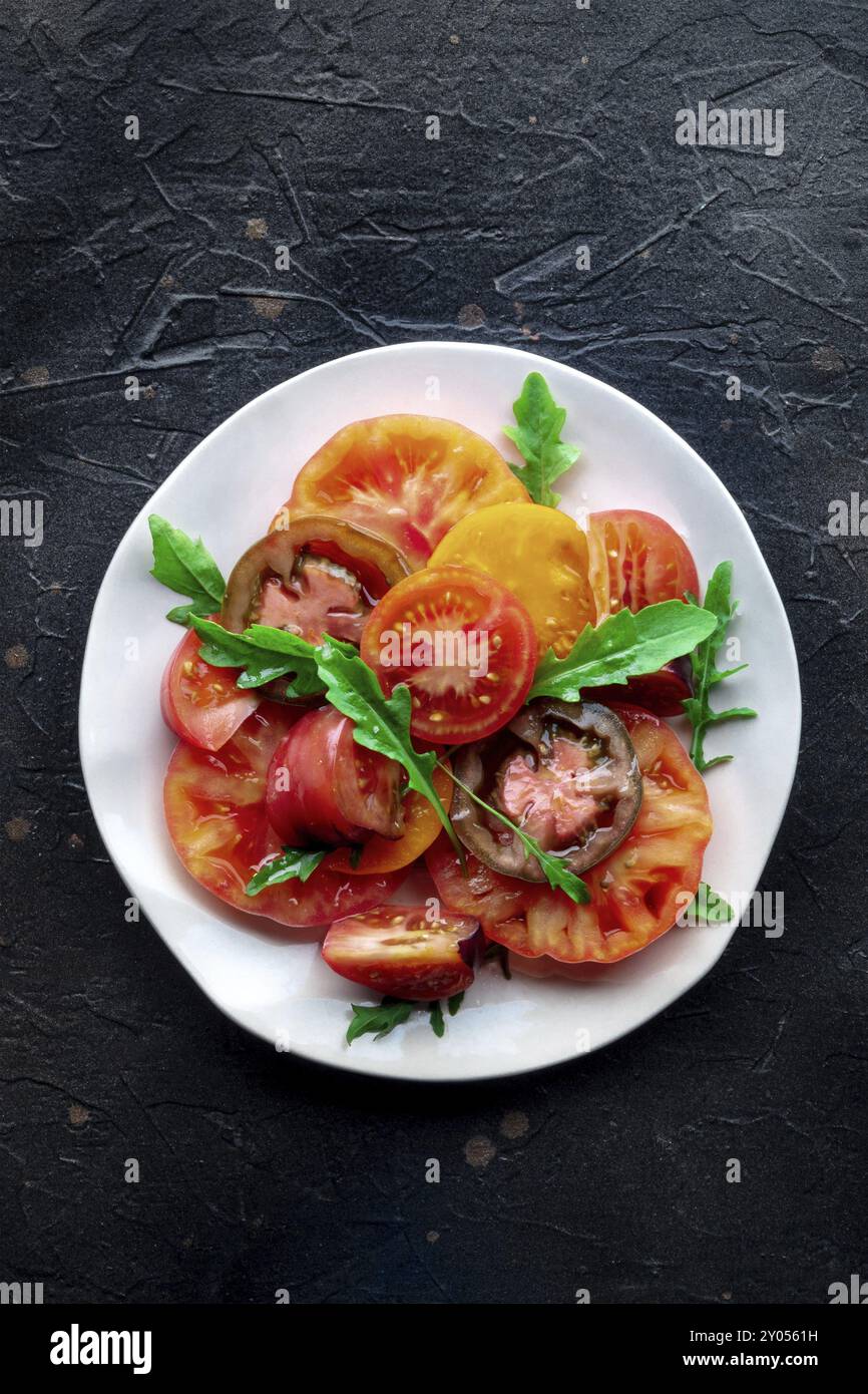 Insalata di pomodoro fresco e rucola. Una varietà di pomodori di diversi tipi, sparati dall'alto con foglie di rucola. Cibo estivo sano, top shot Foto Stock