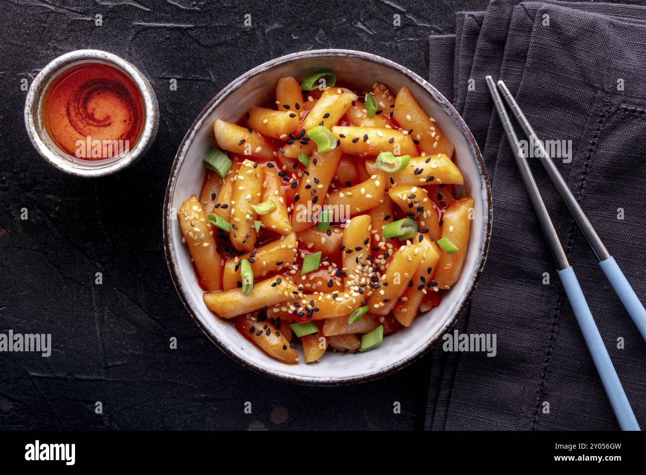 Tteokbokki o topokki, cibo di strada coreano, torte di riso piccanti, shot piatto con bacchette e una bevanda Foto Stock
