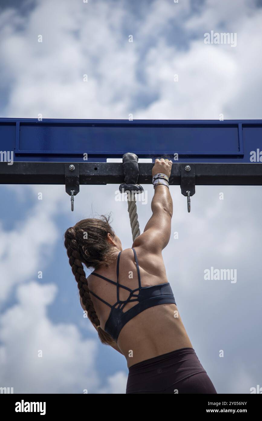 Atleta che sale su una corda durante una gara di fitness all'aperto. L'immagine mostra la donna che ha raggiunto il limite della corda con la forza AN Foto Stock