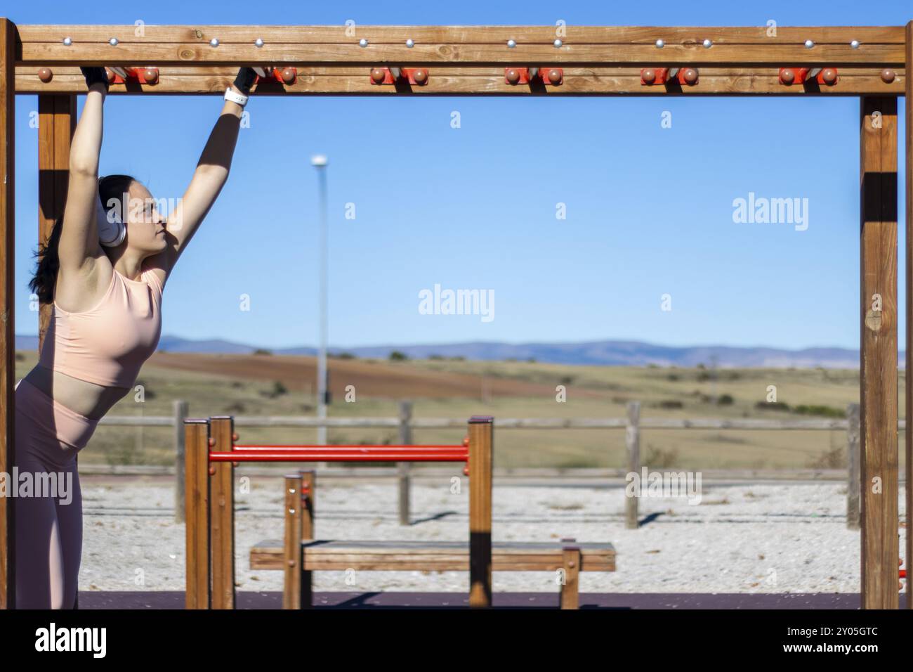 Ritratto di una donna atletica che tira su barre parallele in una giornata di sole con cuffie e abbigliamento sportivo Foto Stock