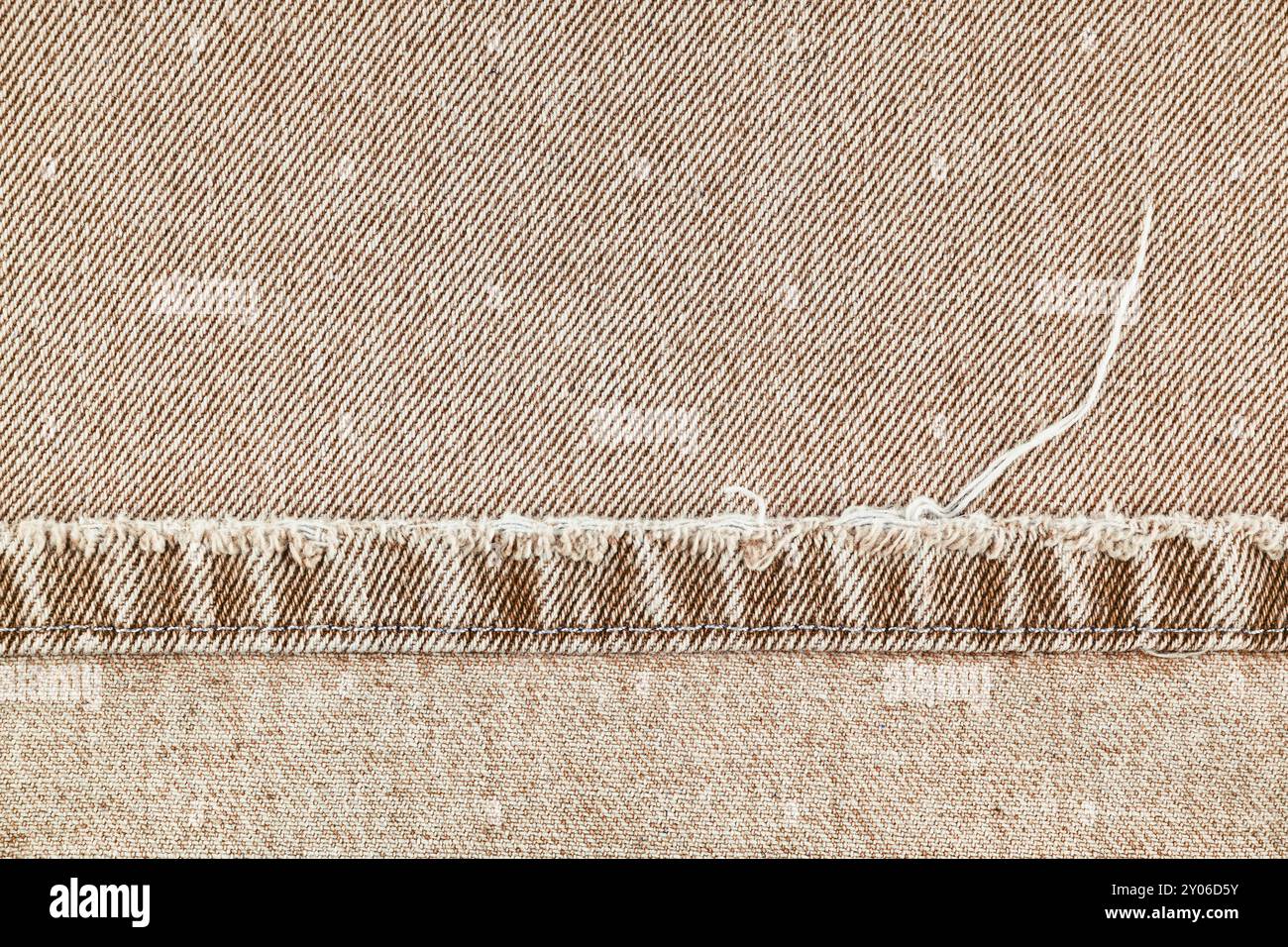 Pantaloni in denim marrone con bordo scabro su fondo in tessuto jean, primo piano, macro. Jeans strappati, distrutti strappati. Sfondo, sfondo, dettagli di design Foto Stock