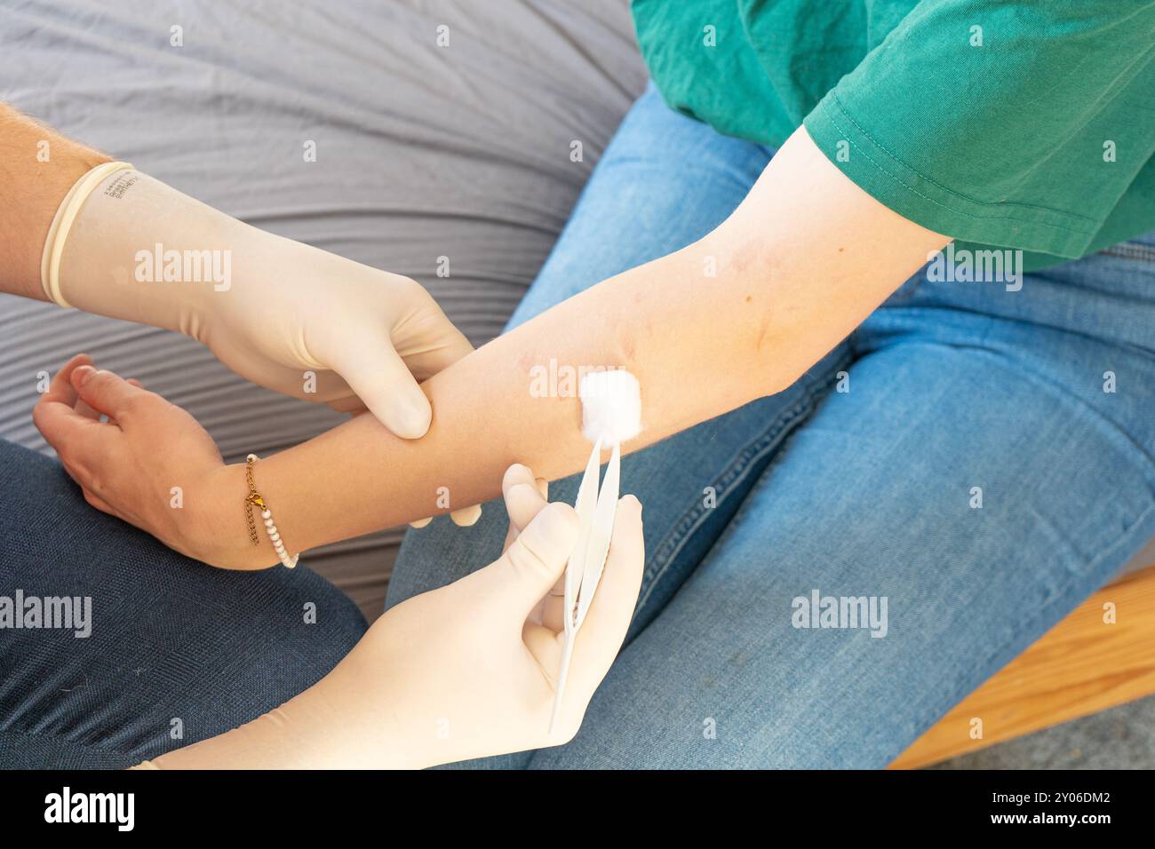 Dottore in abiti semplici braccio curativo di una donna. Cura a casa per una ragazza. Medico senza cappotto bianco con guanti bianchi che danno assistenza medica a casa. Foto Stock