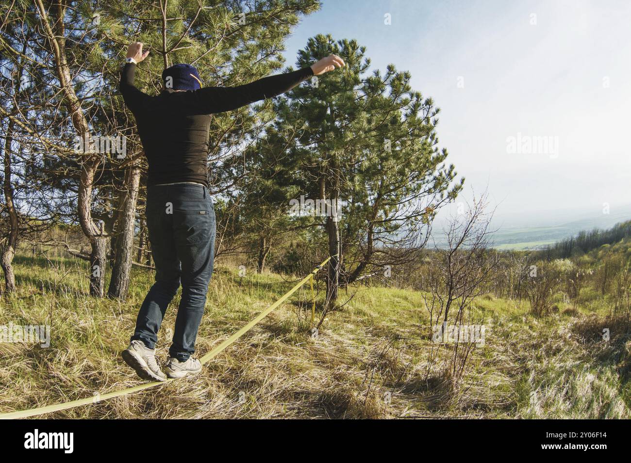 Un uomo, invecchiato con la barba e con gli occhiali da sole, si bilancia su una linea lenta all'aria aperta tra due alberi al tramonto sul cielo blu di sfondo Foto Stock