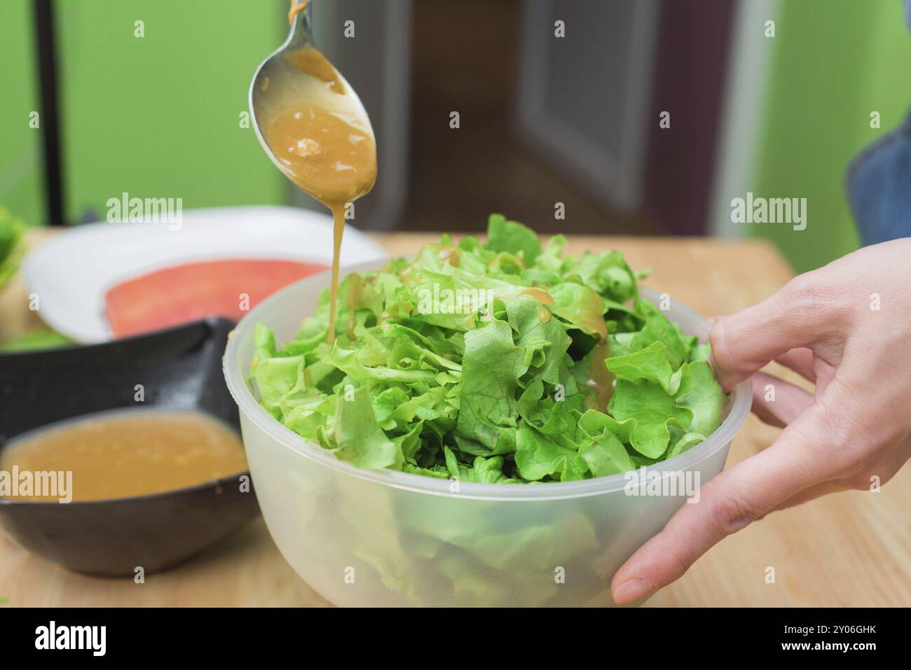 Mani femminili aggiungendo salsa alla lattuga dalle foglie di lattuga. Cucina casala. Cibo sano e gustoso Foto Stock