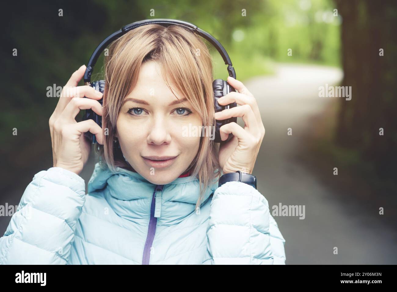 Ritratto di un'attraente bionda sportiva in una giacca leggera che indossa le cuffie bluetooth con musica o i suoni della natura mentre sono in funzione Foto Stock