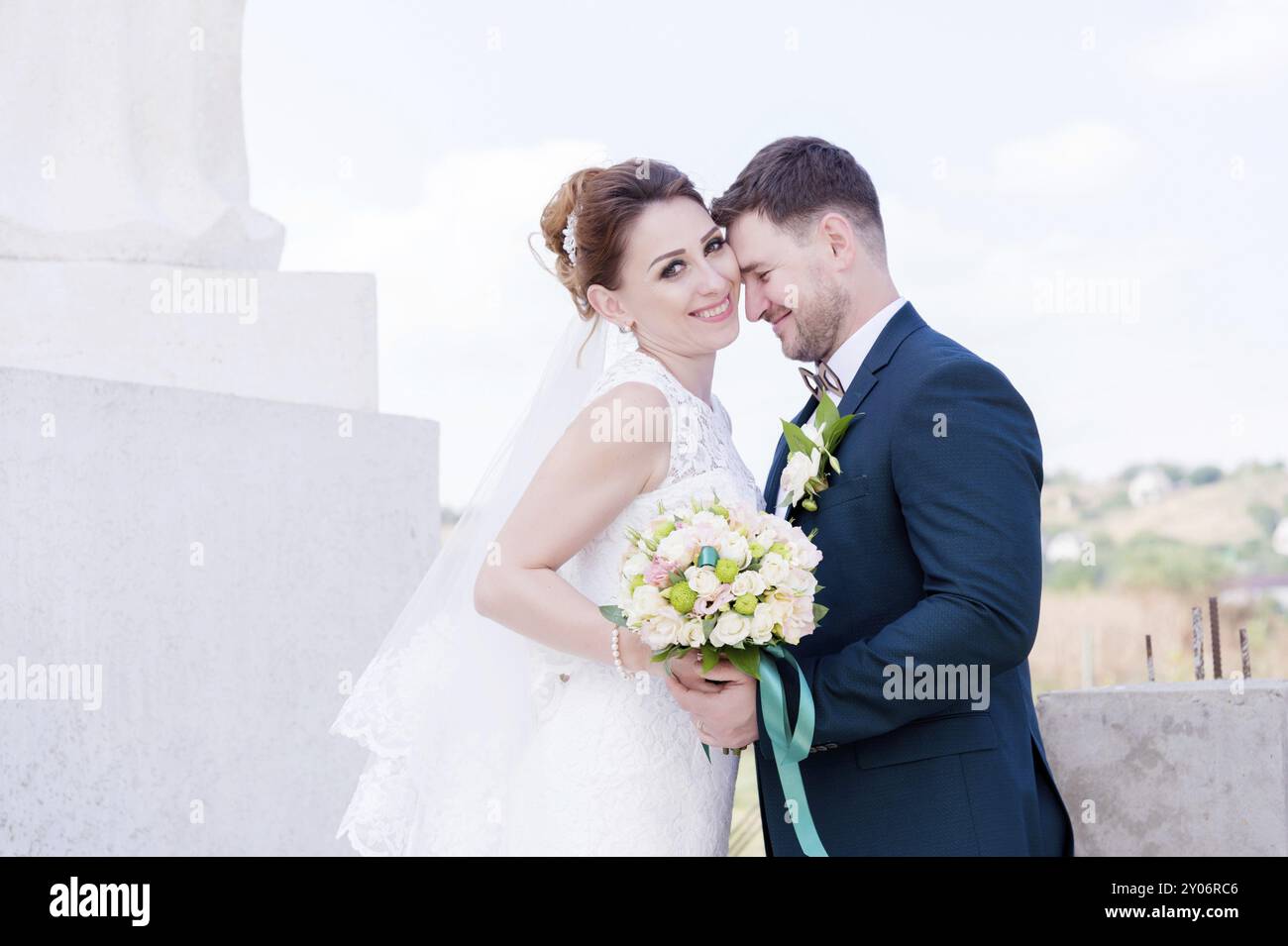 Ritratto di una bella coppia in luna di miele in un giorno di nozze con un bouquet in mano sullo sfondo di un monumento cristiano ortodosso con angeli. Foto Stock