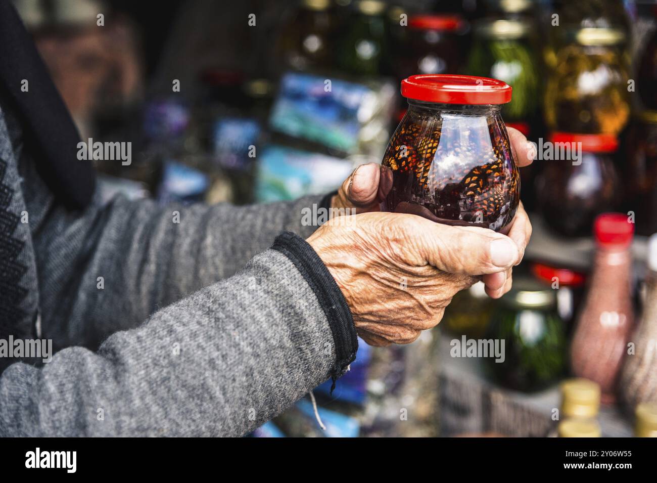 Le mani di una vecchia donna rugosa tengono in mano un barattolo con marmellata fatta in casa di coni in montagna Foto Stock