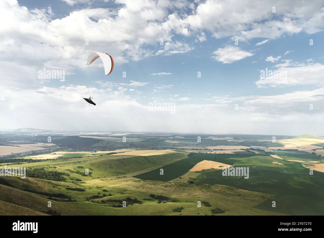 Parapendio bianco arancio con parapendio in bozzolo sullo sfondo di campi del cielo e nuvole. Parapendio Sport Foto Stock