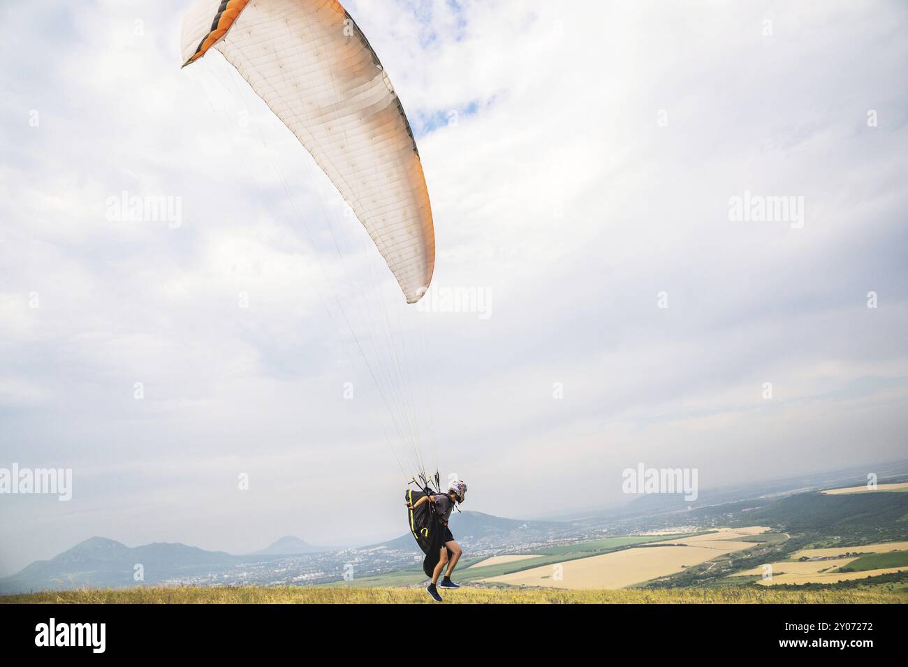 Un parapendio uomo che si decollerà dal bordo della montagna con i campi sullo sfondo. Sport di parapendio Foto Stock