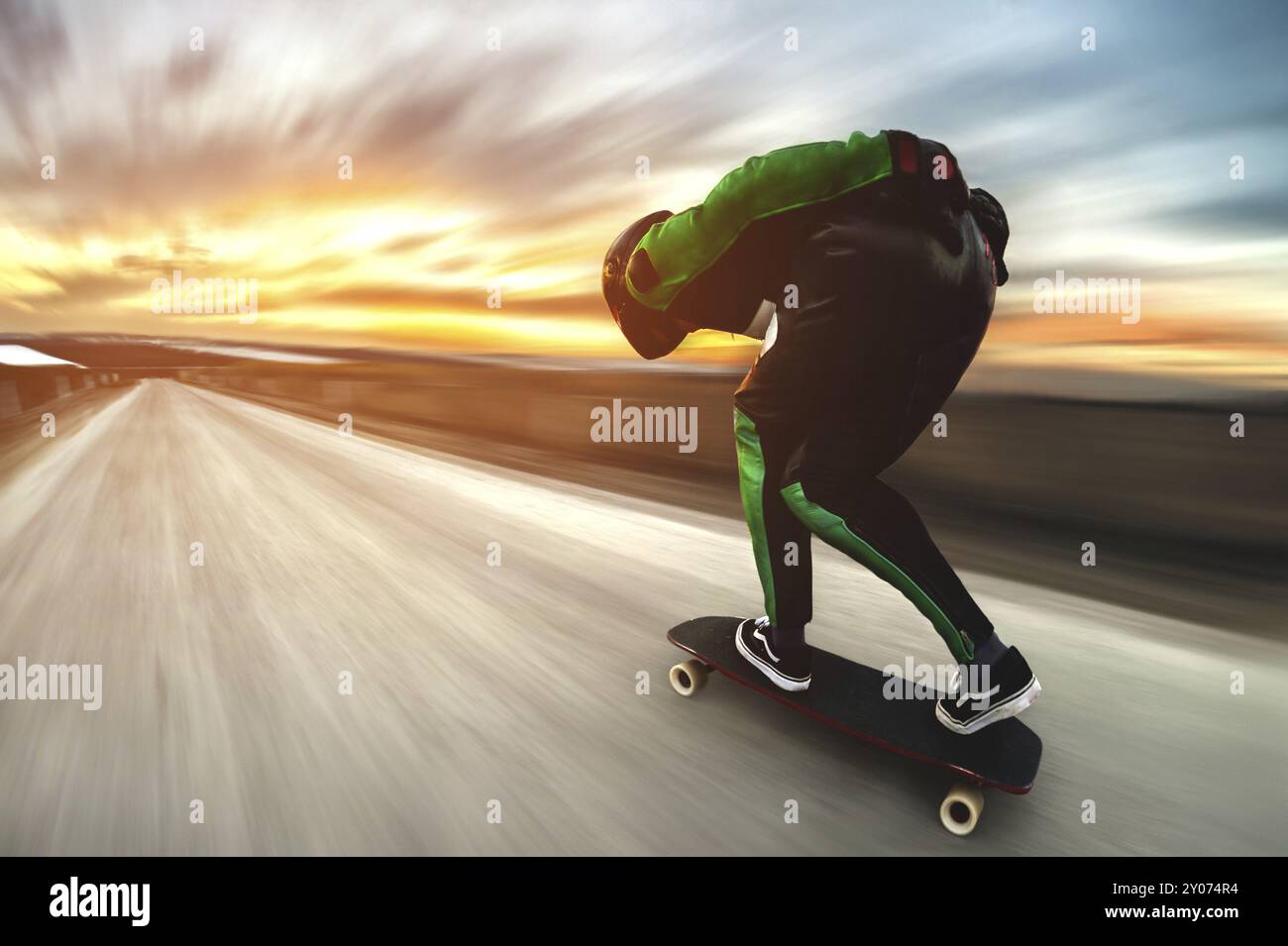 Un uomo con casco e tuta in pelle, in una speciale cremagliera ad alta velocità, cavalca su una lunga longboard per scendere in discesa a galla sullo sfondo di un beauti Foto Stock Un uomo con casco e tuta in pelle, in una speciale cremagliera ad alta velocità, cavalca su una lunga longboard per scendere in discesa a galla sullo sfondo di un beauti Foto Stock