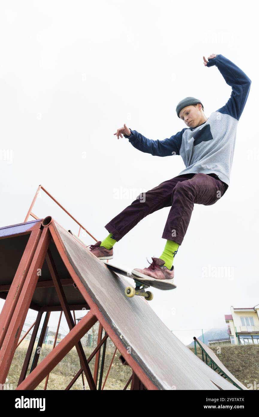 Skater adolescente in felpa con cappuccio e jeans scivola su una ringhiera su uno skateboard in uno skate Park, grandangolare Foto Stock