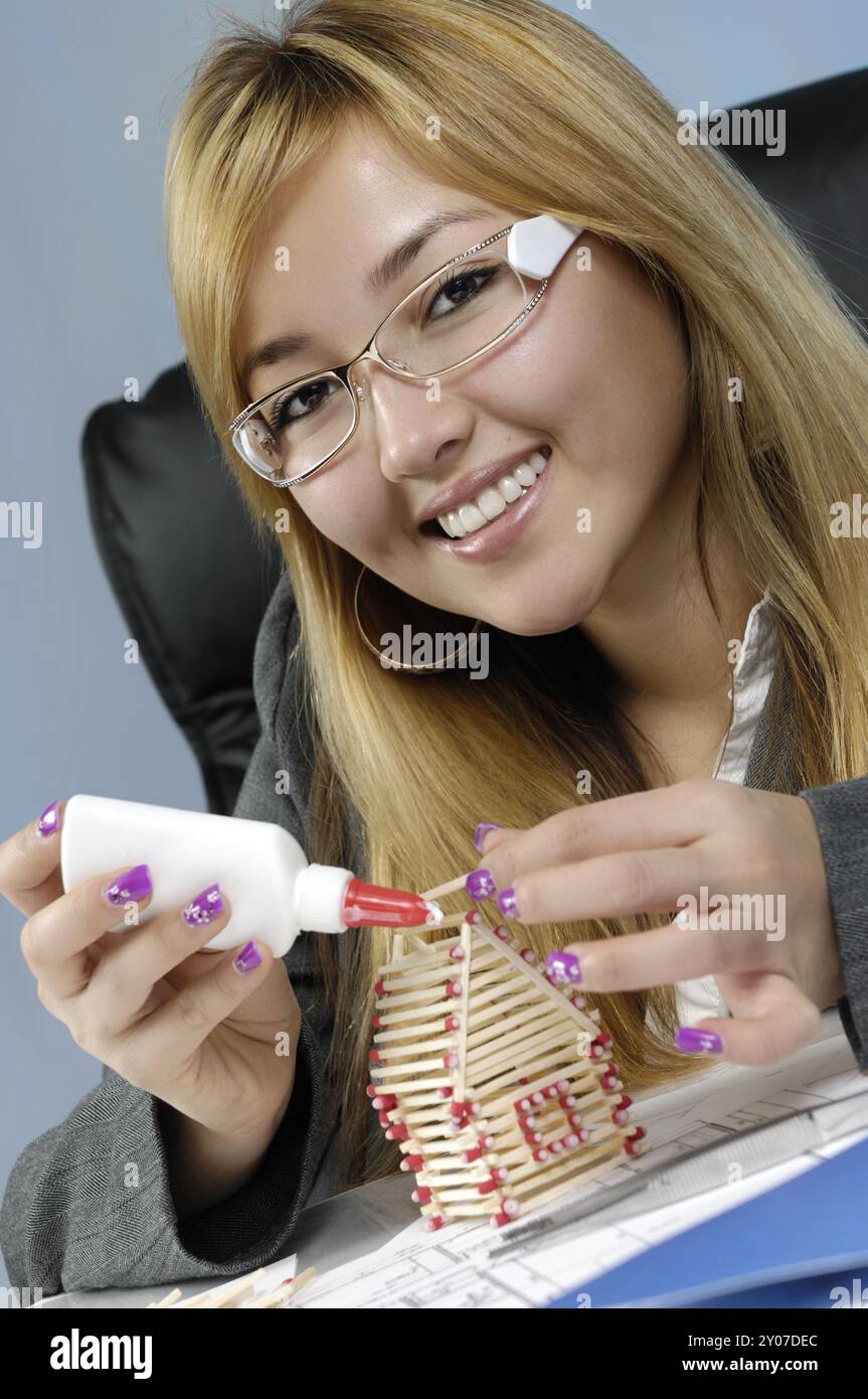 Giovane e attraente donna d'affari che costruisce una casa da fiammiferi. Immobiliare, industria edile, ristrutturazione di abitazioni, progettazione architettonica Foto Stock