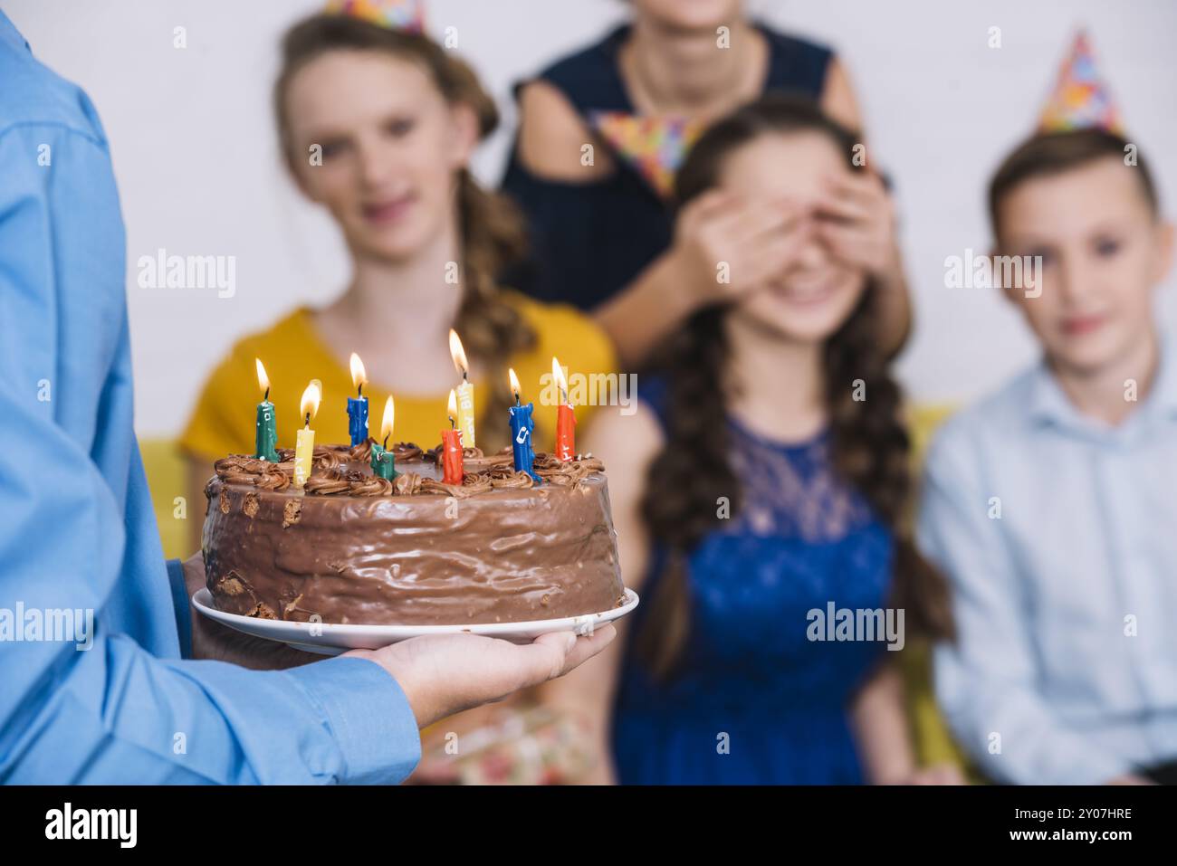 Primo piano la mano del ragazzo portando torta al cioccolato compleanno ragazza con gli occhi coperti dal suo amico Foto Stock