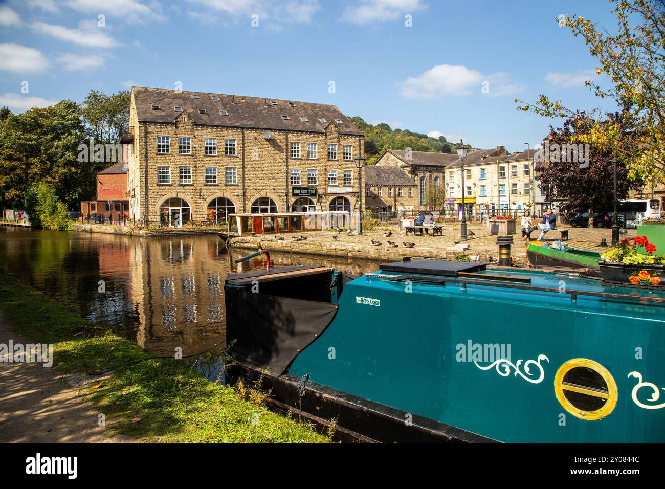 La barca stretta del canale è ormeggiata lungo gli ex edifici del pontile sul canale di Rochdale nella Calder Valley, città mercato dello Yorkshire occidentale, di Hebden Bridge Foto Stock