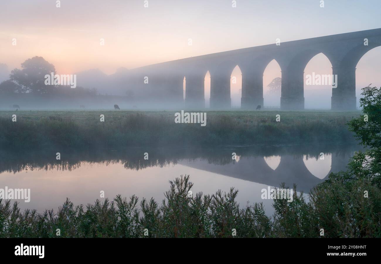 La nebbia copre il paesaggio che circonda il viadotto di Arthington a Wharfedale, nel North Yorkshire, con la scena che si riflette nel tranquillo fiume Wharfe. Foto Stock