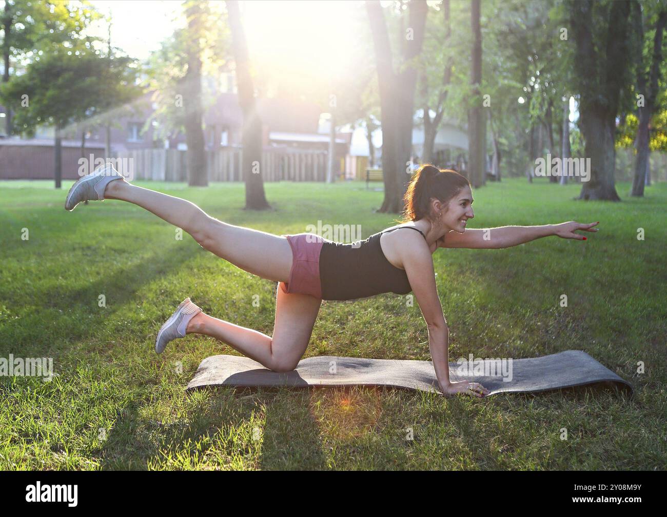 Donna che si allunga in un esercizio all'aperto sorridente felice facendo stretching dopo la corsa. Splendido modello sportivo sorridente all'aperto al tramonto d'estate Foto Stock