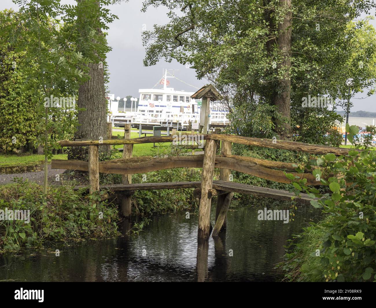 Piccolo ponte di legno su un ruscello con una recinzione di legno in primo piano e una nave sullo sfondo, Bad Zwischenahn, ammerland, germania Foto Stock Piccolo ponte di legno su un ruscello con una recinzione di legno in primo piano e una nave sullo sfondo, Bad Zwischenahn, ammerland, germania Foto Stock