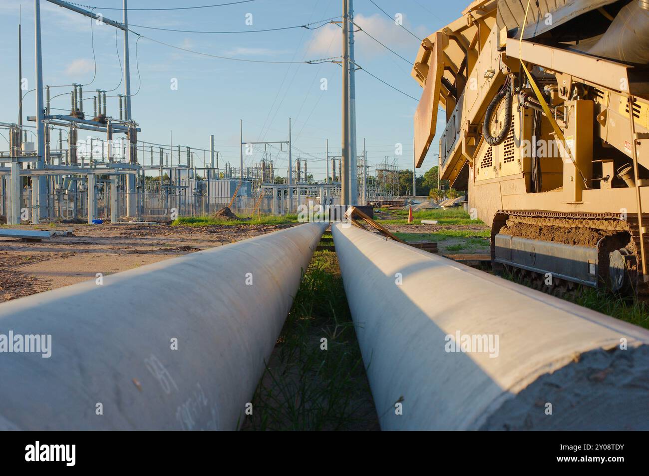 Linea anteriore orizzontale ad angolo basso di due grandi poli metallici sul terreno. Macchina per aggregazione impilatrice alimentatore trasportatore giallo a destra Foto Stock