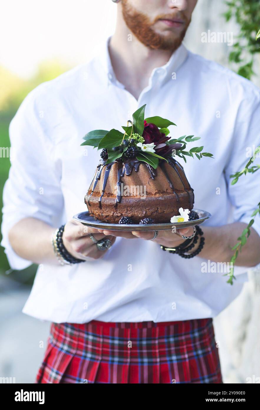 Lo sposo tenendo la torta al cioccolato decorata con blackberry fresca e fiori oin le mani Foto Stock