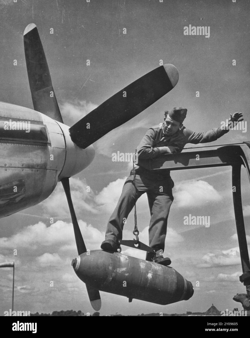 A bordo di una bomba da demolizione da 500 libbre per mantenerla stabile alla fine di una gru, c'è il comandante Lloyd Shumway, Istrouma, La., Ordnance armament man presso una stazione di caccia USAAF North American P-51 Mustang in Inghilterra, circa 1944 Foto Stock