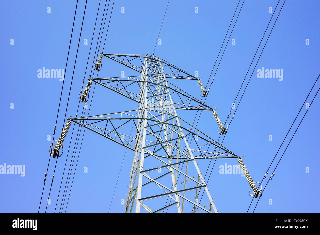 Un alto pilone elettrico metallico supporta più set di cavi elettrici, essenziali per la trasmissione di elettricità, cielo azzurro senza nuvole. Foto Stock