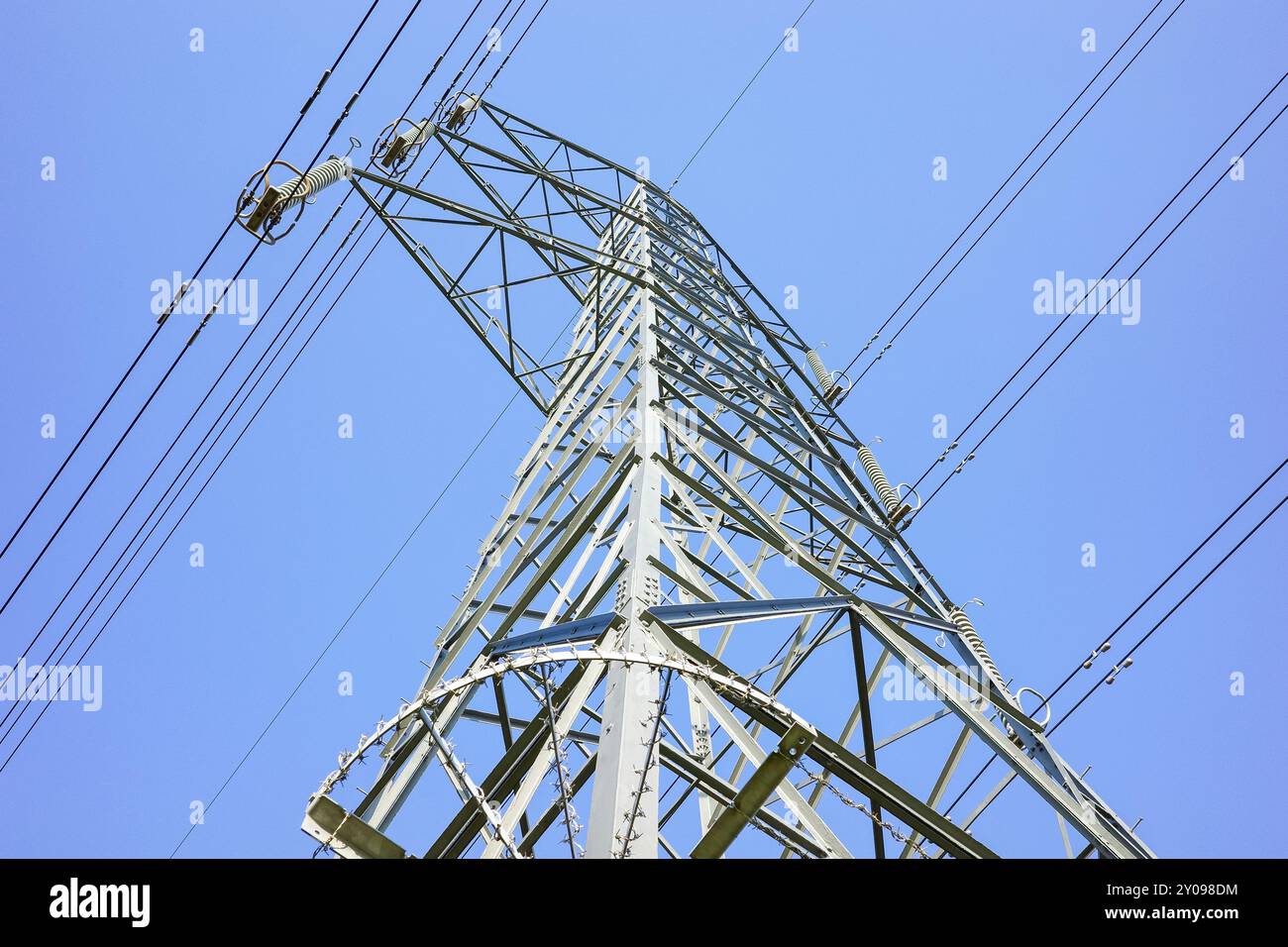 Un alto pilone elettrico metallico supporta più set di cavi elettrici, essenziali per la trasmissione di elettricità, cielo azzurro senza nuvole. Foto Stock
