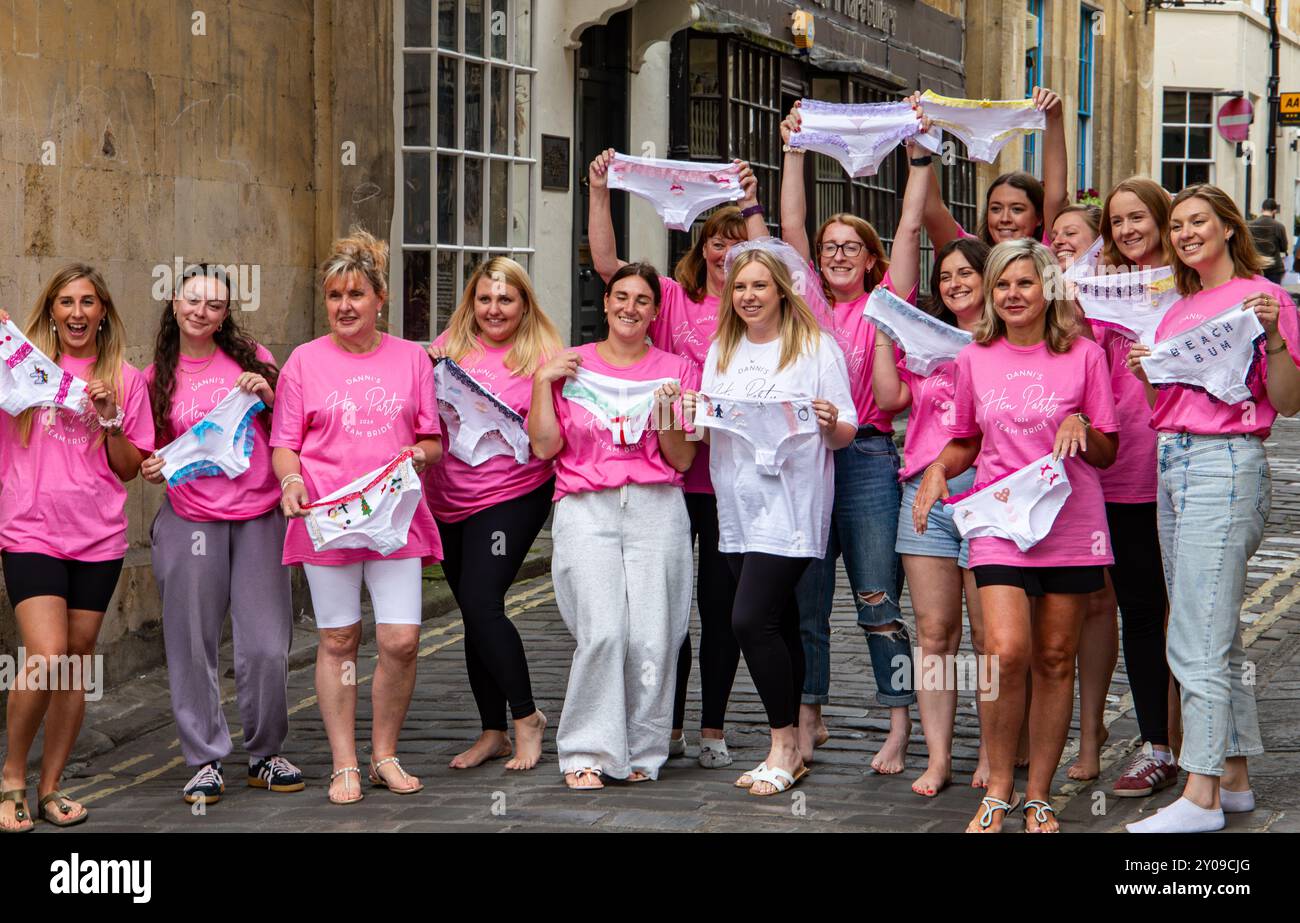 Un gruppo di donne in un giorno di nozze che indossa camicie rosa e tiene in mano abiti personalizzati mentre posa in una stretta strada cittadina a Bath, Inghilterra. Foto Stock