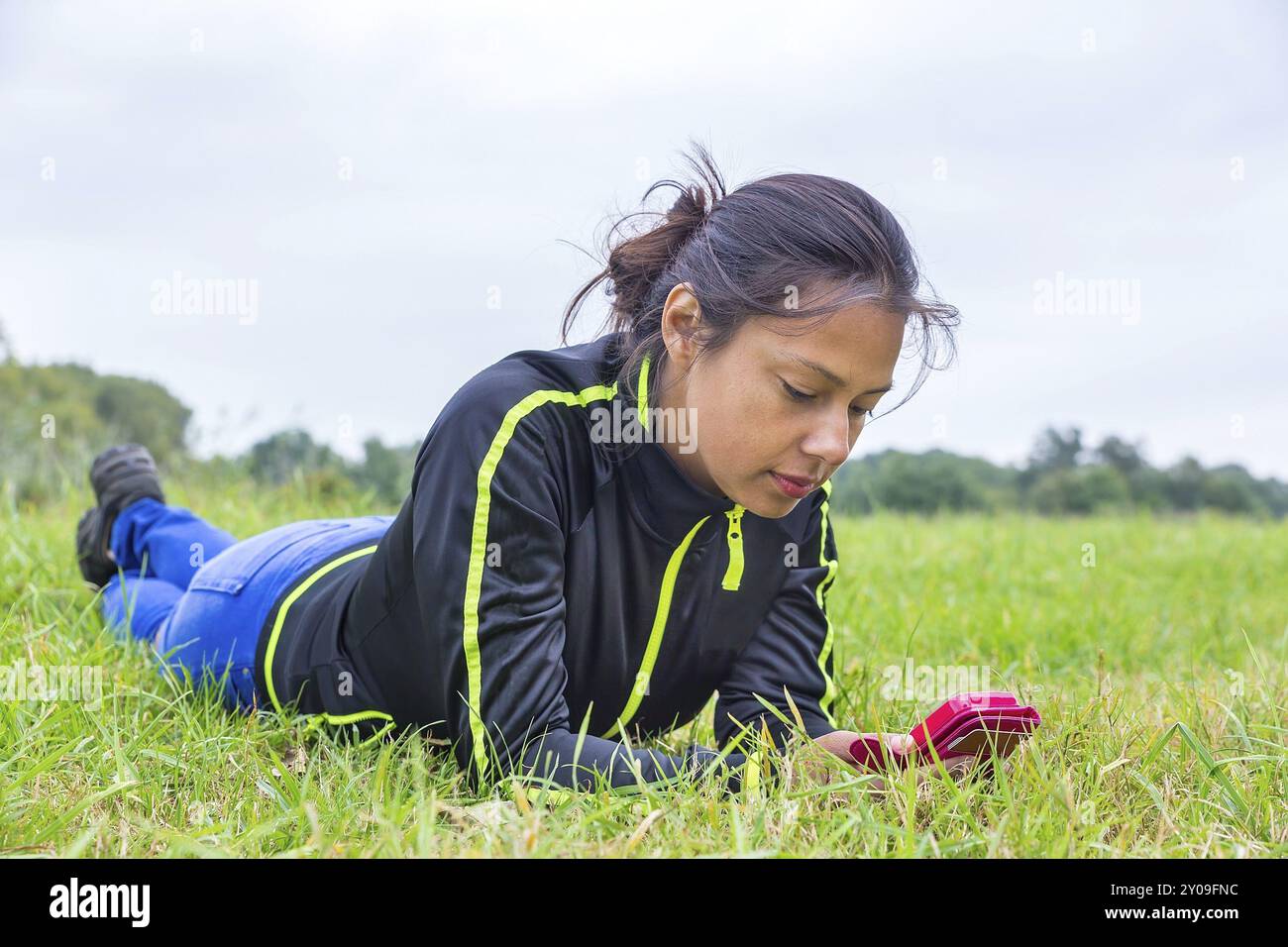 Giovanissimo colombiano donna sdraiata nel prato di funzionamento del telefono mobile Foto Stock