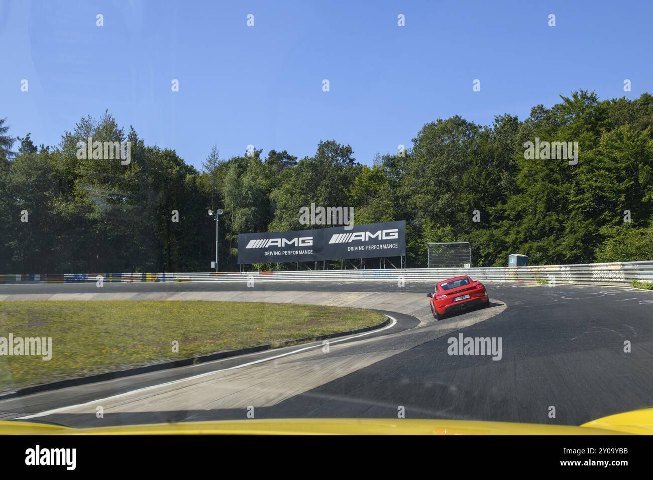 Vista dall'auto da corsa su un'auto sportiva rossa Porsche Cayman attraversa la sezione Caracciola-Karrussell della pista stretta curva con ripida pendenza di Nuerburg Foto Stock