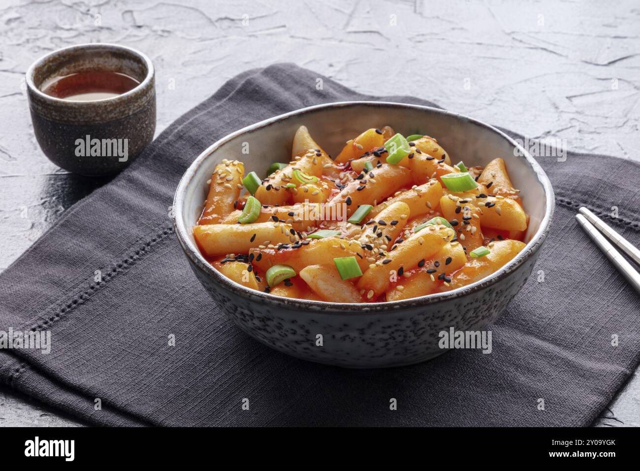 Tteokbokki o topokki, Street food coreano, torte di riso piccanti in salsa gochujang al peperoncino rosso, un piatto popolare, con una bevanda Foto Stock