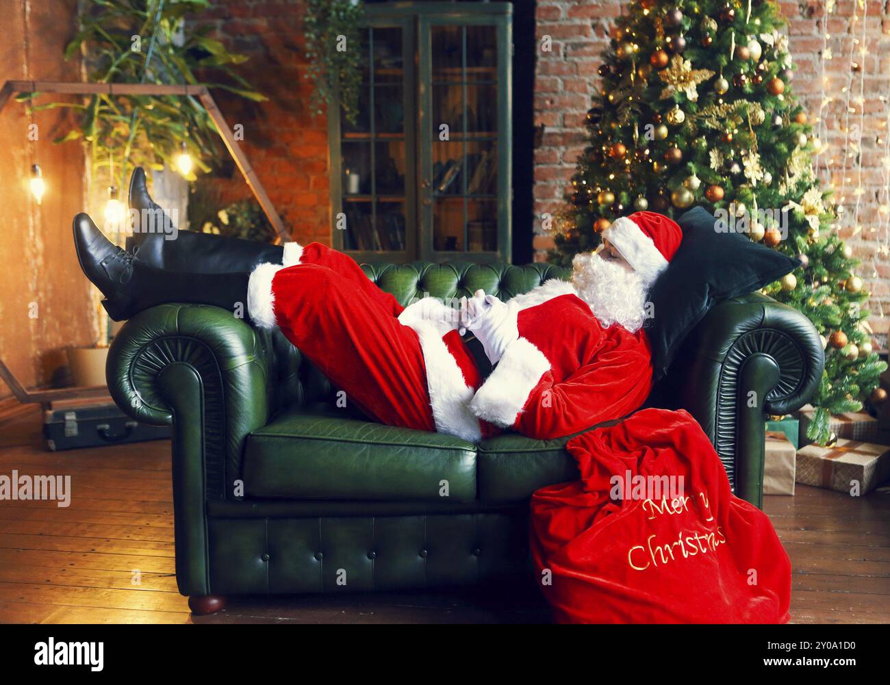 Santa Claus dormono a casa nei pressi di albero di Natale sul divano verde Foto Stock