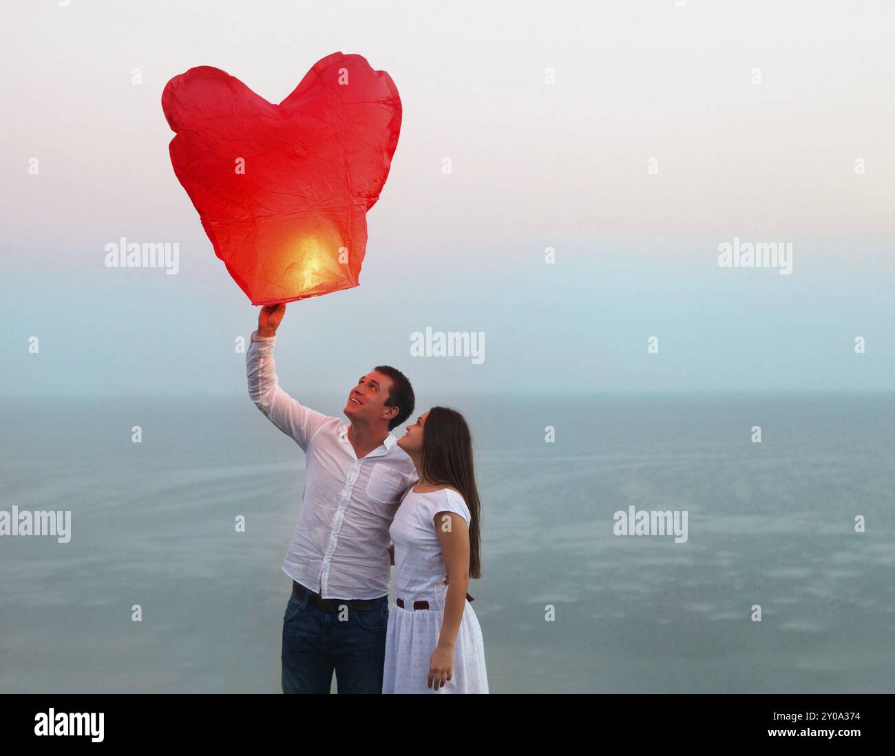 Coppia giovane iniziare un rosso cielo cinese lanterna nel tramonto vicino al mare Foto Stock