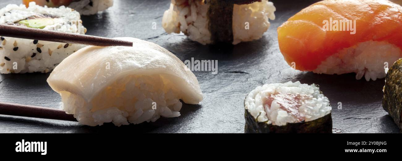 Sushi con panorama con bacchette. Nigiri di pesce bianco su sfondo nero, cibo giapponese su un piatto in un ristorante asiatico, fotografia gastronomica Foto Stock