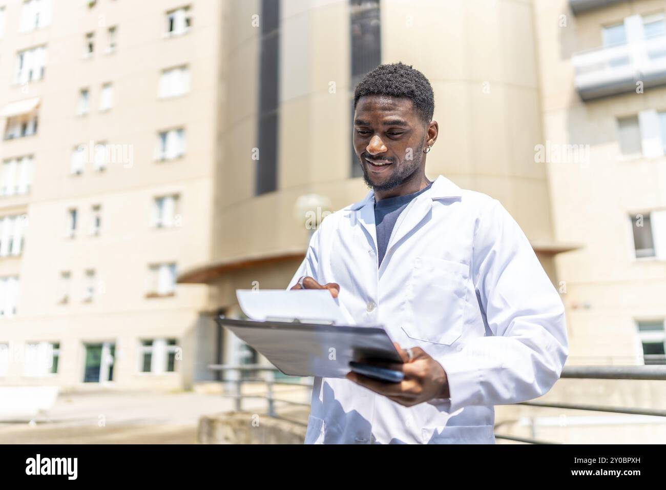 Giovane medico africano che controlla le cartelle cliniche fuori dall'ospedale sotto il sole Foto Stock