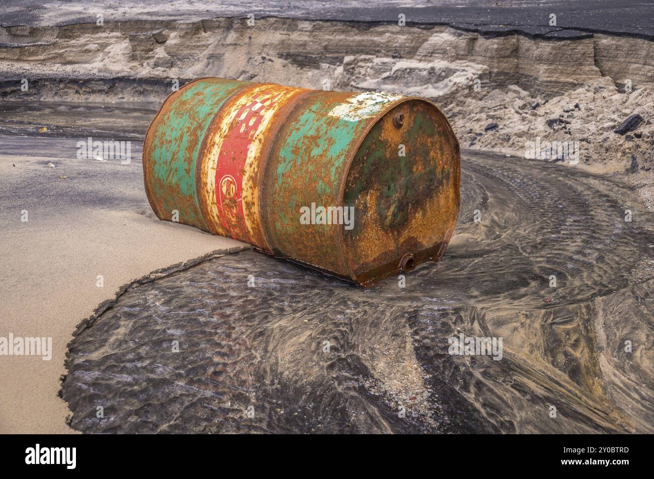 L'olio per fusti arrugginito su una spiaggia di colore parzialmente nero illustra l'inquinamento ambientale causato dalle fuoriuscite di petrolio Foto Stock