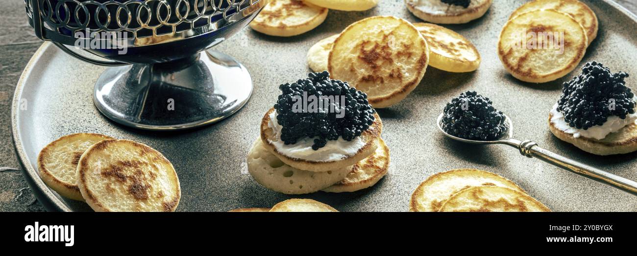 Blinis con panorama caviale nero. Mini pancake su un piatto festivo, un elegante antipasto, fotografia gastronomica Foto Stock