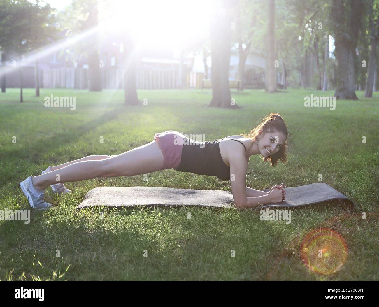 Donna che si allunga in un esercizio all'aperto sorridente felice facendo stretching dopo la corsa. Splendido modello sportivo sorridente all'aperto al tramonto d'estate Foto Stock