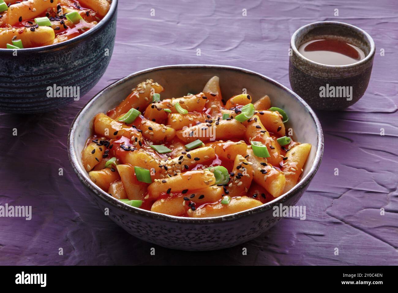 Tteokbokki o topokki e rabokki, Street food coreano, torte di riso piccanti in salsa gochujang al peperoncino rosso, un piatto popolare, con una bevanda Foto Stock