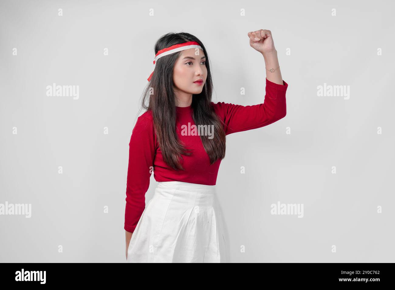 Attraente giovane donna asiatica con una camicia rossa e pantaloni bianchi sorride e alza la mano in aria. Indonesia Independence Day Concept. Foto Stock