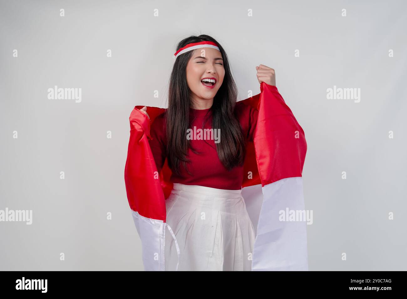 La giovane donna asiatica allegra tiene la bandiera indonesiana alle spalle e solleva pugni in aria con un'espressione felice di successo. Independen indonesiano Foto Stock