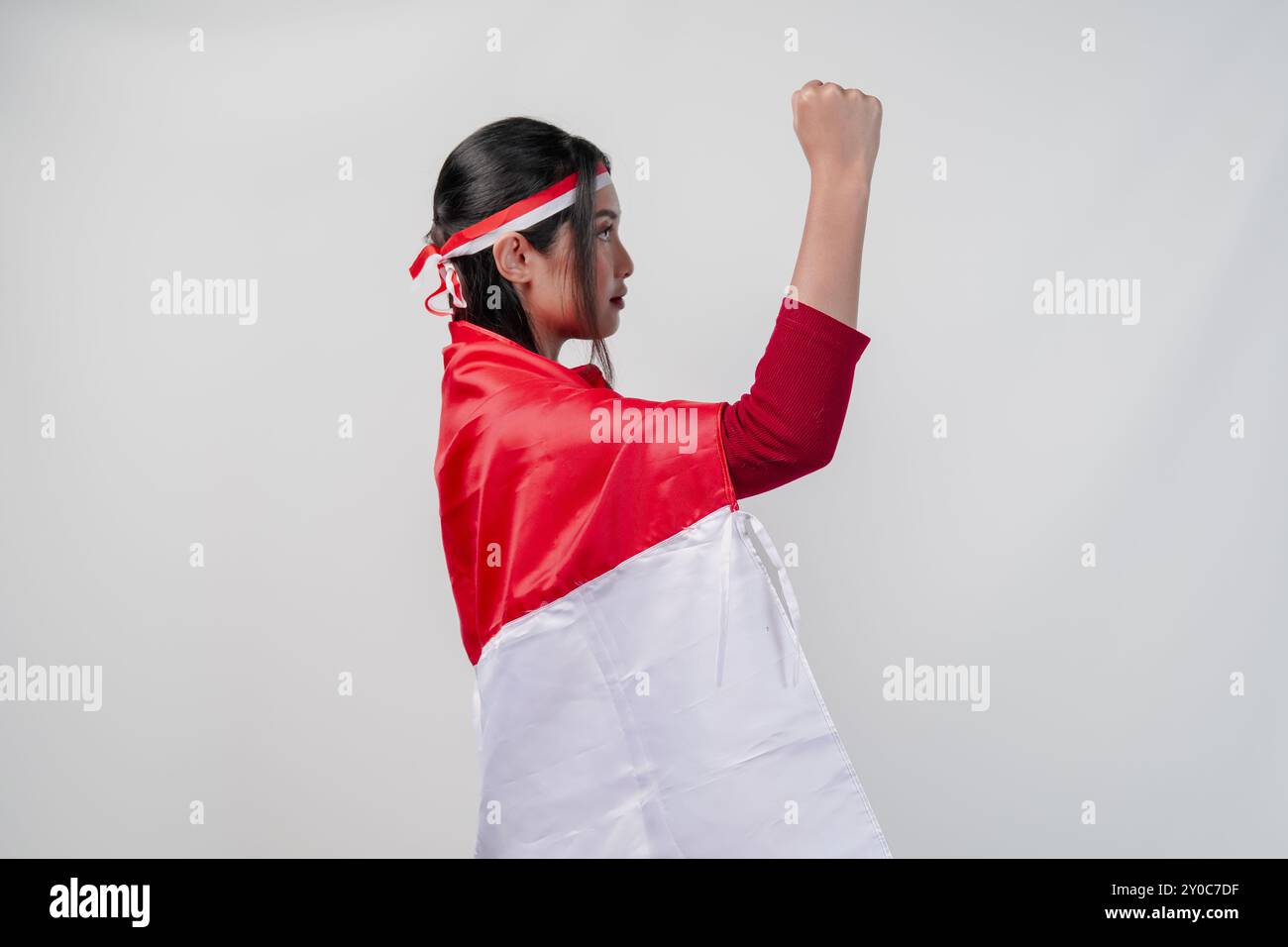 Ritratto laterale di donna asiatica che si copre di bandiera indonesiana e tiene il pugno in alto in aria. Indonesia Independence Day Concept. Foto Stock