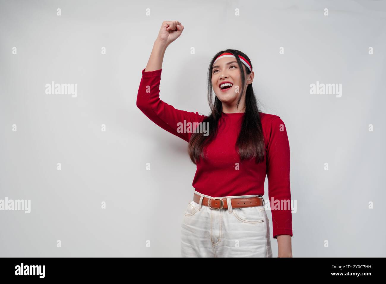 Allegra giovane donna asiatica con una camicia rossa e pantaloni bianchi sorride e alza la mano in aria. Indonesia Independence Day Concept. Foto Stock