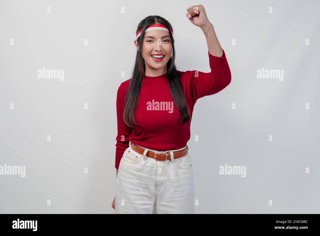 Attraente giovane donna asiatica con una camicia rossa e pantaloni bianchi sorride e alza la mano in aria. Indonesia Independence Day Concept. Foto Stock