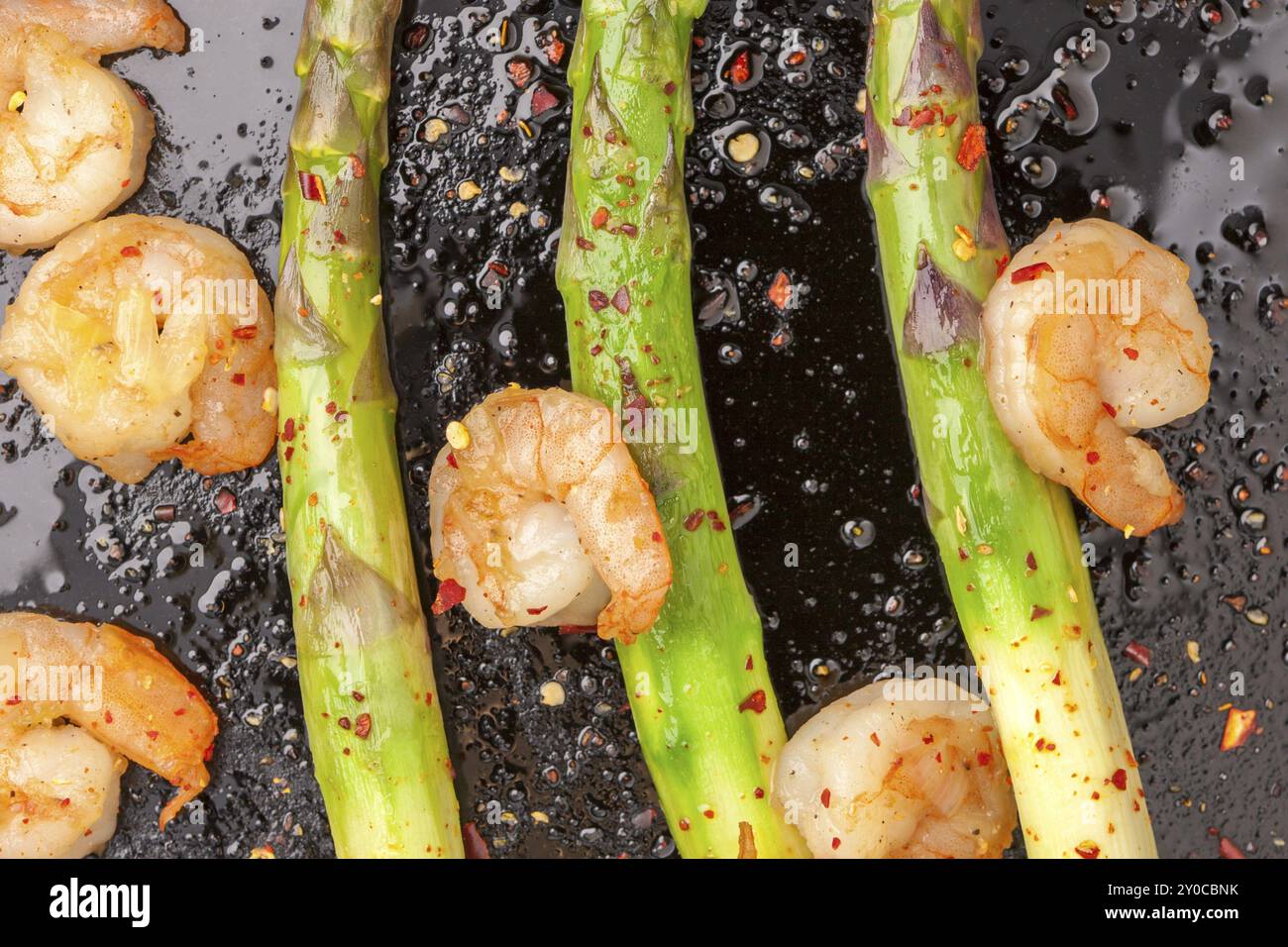 Asparagi con gamberi conditi in una padella di ghisa ricoperta di peperoni rossi tritati Foto Stock