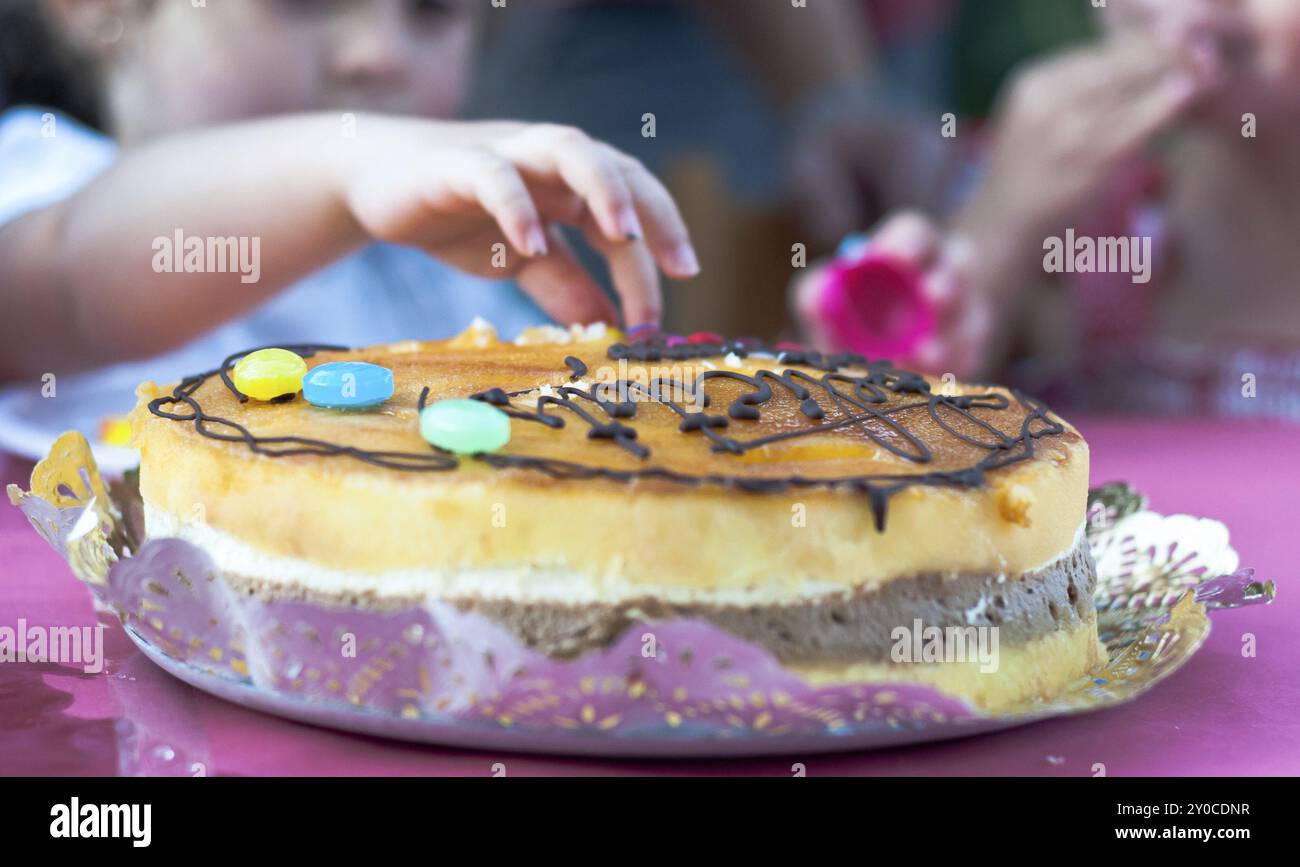 I bambini toccano una torta di compleanno festosa con decorazioni colorate di caramelle, catturando un momento di gioco Foto Stock