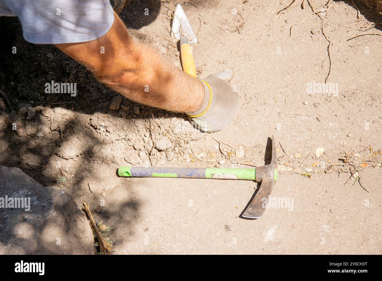 braccio di un archeologo in uno scavo archeologico sul lato del pavimento ci sono due attrezzi, una piccola piccone e una cazzuola. Foto Stock